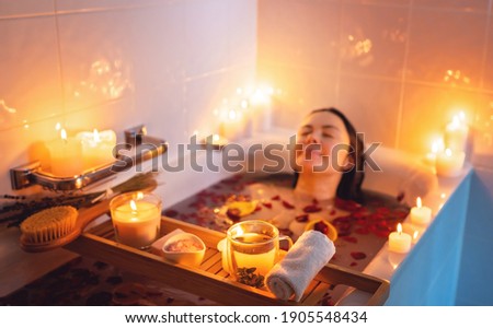 Young woman enjoying spiritual aura cleansing rose flower bath with rose petals and candles during full moon ritual. Body care and mental health routine.  Royalty-Free Stock Photo #1905548434