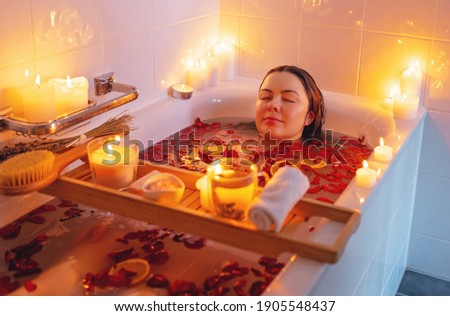 Young woman enjoying spiritual aura cleansing rose flower bath with rose petals and candles during full moon ritual. Body care and mental health routine.  Royalty-Free Stock Photo #1905548437