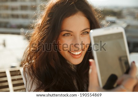 beautiful, smiling woman take a picture of herself with a smartphone. selfie, outdoors shot, horizontal 