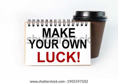 MAKE YOUR OWN LUCK, text on white paper on white background. On the background of cups with coffee