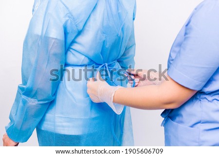 Enlarged photo of the hands of a nurse tie a disposable gown to a patient preparing for hospitalization. Royalty-Free Stock Photo #1905606709