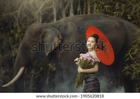 The girl and the elephant are carrying flowers.Beautiful young Asian woman dressed in traditional native dress and elephant in forest of village Surin Thailand 