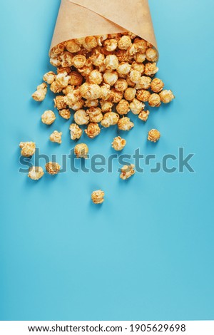 Caramel popcorn in a paper envelope on a blue background. Delicious praise for watching movie movies, serial, cartoon. Free space, close-up. Minimalistic concept.