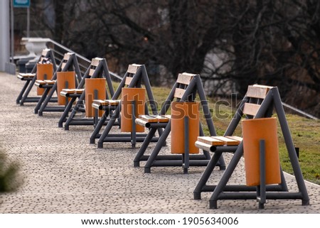 Row of empty new wooden benches and garbage bins on a sidewalk in a city park.
