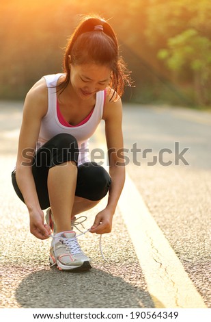 young fitness woman tying shoelaces on road 