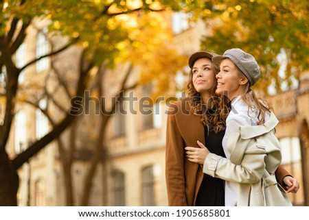 Two girls walking in city park and smilling. Autumn picture