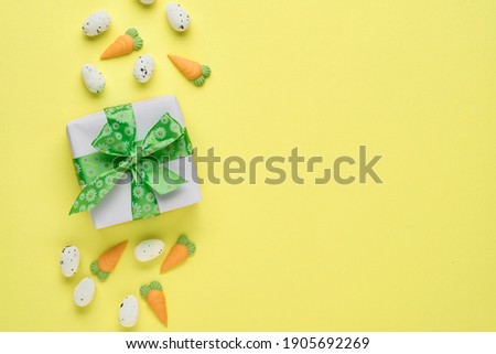 Easter spring greeting card with gift box with green ribbon, eggs and sweet carrot on pink background. Top view.