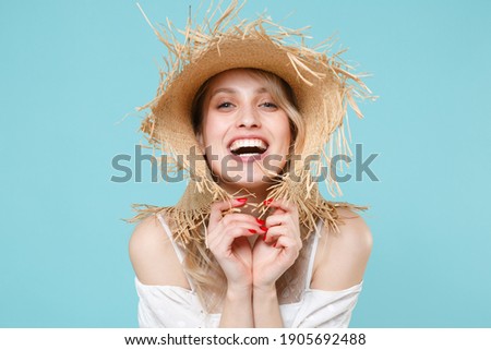 Laughing cheerful charming beautiful attractive young blonde woman 20s wearing white summer dress hat standing and looking camera isolated on blue turquoise colour background, studio portrait