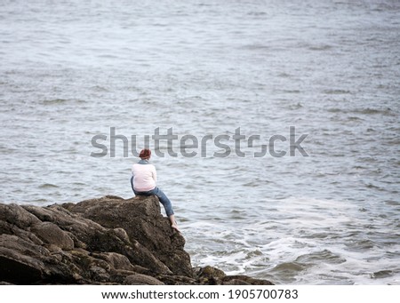Alone woman sitting on the rocks by the sea view. View from the back, Faceless, Without a face.