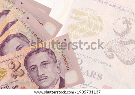 2 Singaporean dollars bills lies in stack on background of big semi-transparent banknote. Abstract business background