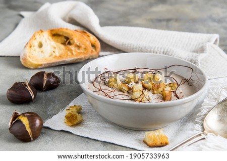 Chestnut soup with parmesan, croutons and chilli flakes and threads on grey concrete background, decorated with roasted bread and chestnuts Royalty-Free Stock Photo #1905733963