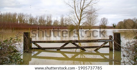 Flood water in fields, UK countryside, 2021. Climate change, extreme weather, global warming. Global floods risk under climate change. Flooded wooden filed gate Royalty-Free Stock Photo #1905737785
