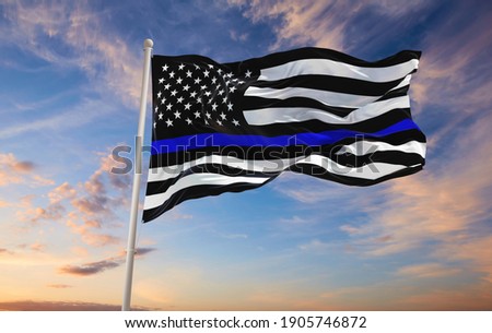 Thin Blue Line. Black Flag of USA with Police Blue Line waving in the wind on flagpole against the sky with clouds on sunny day