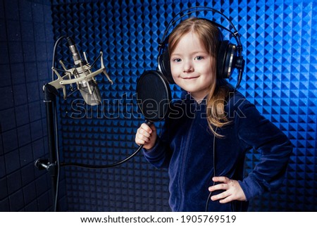 girl star singer artist in a black blouse with headphone recording new song with microphone.
