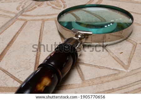 Angled closeup of a vintage magnifying glass on intricate beige tile. 