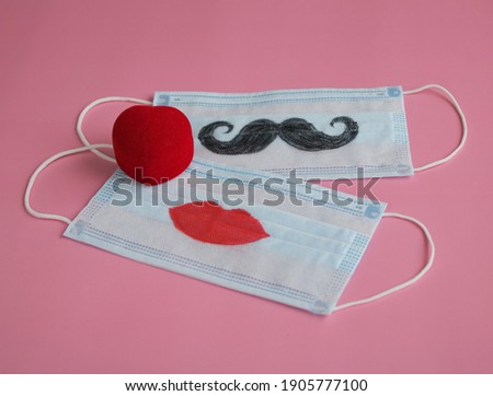 The gift box for engagement ring next to disposable protective masks with painted mustache and lips on pink background. The concept of St. Valentine's Day, wedding etc during pandemic of COVID-19