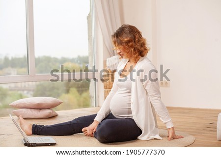 Pregnancy, beautiful young pregnant European woman sitting at home in a bed in white clothes, motherhood, waiting for the birth of a child.

