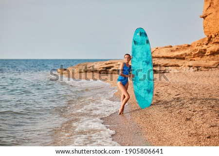 Ocean view and sandy beach. Lady in swimsuit with surfboard. Surf hobby, summer vacation and adventure idea. Copy space