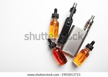 Vape juice next to smoking devices. Bottles with vape juice on a white table. Devices for vaping and vape juice nearby. Top view vaper set. E-cigarette refills. Liquids for vaping devices Royalty-Free Stock Photo #1905813715