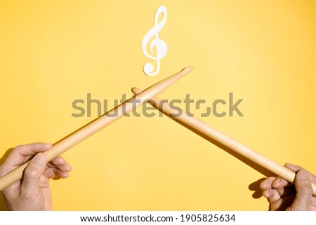 Drummer concept. Male hands holding drumsticks and a paper treble clef and musical treble clef. Flat lay