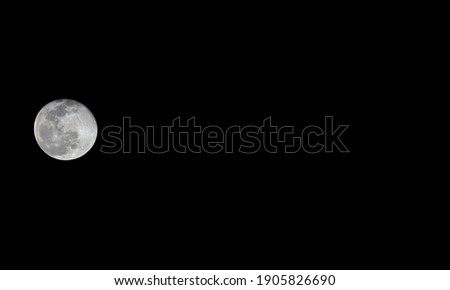 A bright moon on a pitch black sky with copy space on the side for text.