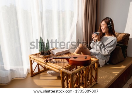 A beautiful young asian woman enjoy drinking coffee and listening to music with headphone at home, happiness and relaxation concepts