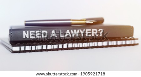 On the table are a notebook, a pen and a book. The book says - NEED A LAWYER
