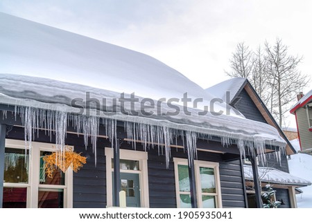 Gabled roof of home covered with thick snow and lined with icicles in winter Royalty-Free Stock Photo #1905935041