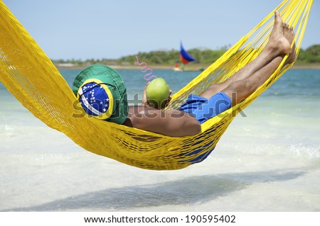 Brazilian man relaxing in beach hammock drinking fresh coconut water coco verde gelado