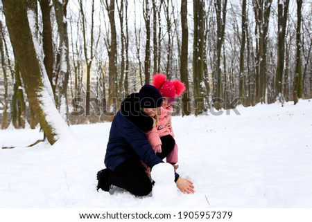 Mom and her little daughter in the winter sculpt a snowman in a snowy forest