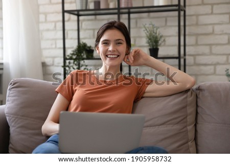Portrait overjoyed woman with laptop sitting on cozy couch at home, smiling attractive female looking at camera, holding computer on laps, enjoying leisure time, having fun with device, social media