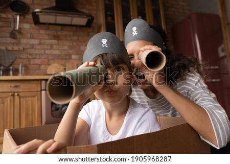 Head shot portrait happy mother and little daughter playing pirates, looking at camera, excited mum and preschool gild child wearing handmade costumes, holding paper tubes as spyglass, having fun