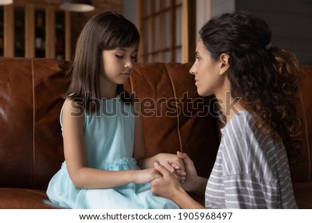 Close up caring young mother comforting calming upset offended little daughter, holding hands, sitting on couch, mum expressing love and support, child psychologist concept, psychological help Royalty-Free Stock Photo #1905968497