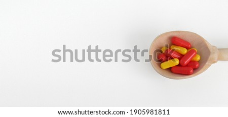 
wooden spoon with pills in the form of capsules on a white background