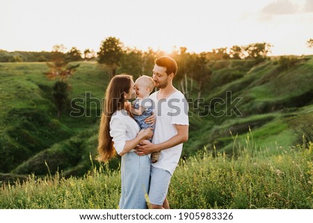 Young beautiful family with a little daughter hug, kiss and walk in nature at sunset. Photo of a family with a small child in nature. Royalty-Free Stock Photo #1905983326