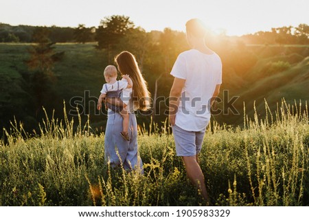 Young beautiful family with a little daughter hug, kiss and walk in nature at sunset. Photo of a family with a small child in nature. Royalty-Free Stock Photo #1905983329