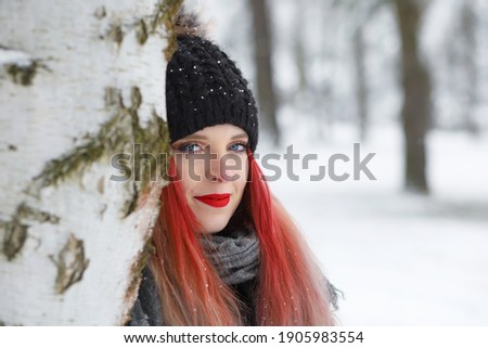 Portrait of attractive red hair girl behind a birch tree smiling at the camera. Horizontally.