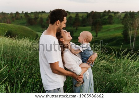 Young beautiful family with a little daughter hug, kiss and walk in nature. Photo of a family with a small child in nature. Royalty-Free Stock Photo #1905986662
