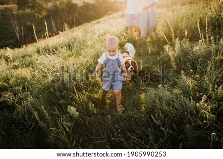 A young beautiful family with a little daughter and a dog hug, kiss and walk in nature. Close-up of a little girl walking near her parents in nature.