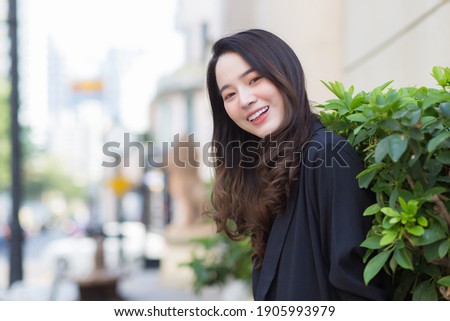 Portrait Asian woman with long hair wears black coat and stands outdoor in town.
