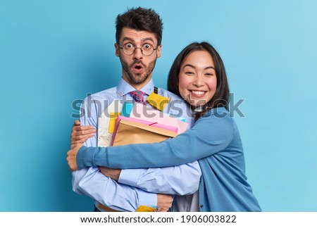 Cheerful Asian woman embraces her groupmate expresses support to best friend congratulates with successfully passed final exam. Mixed race students prepare for seminar. People paper work concept Royalty-Free Stock Photo #1906003822