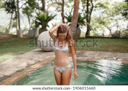 Summer vacation concept. Young woman wearig swimsuit stand near swimming pool surrounded with tropical landscape