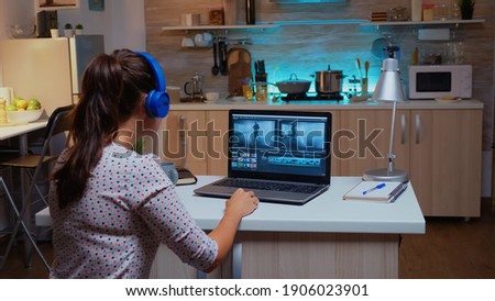 Professional colorist working in video footage during post production. Videographer editing audio film montage on modern device, laptop sitting on desk in modern kitchen in midnight