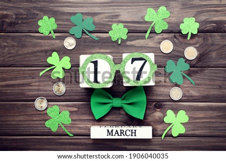 St.Patrick's Day. Paper clover leafs with coins and cube calendar on wooden table