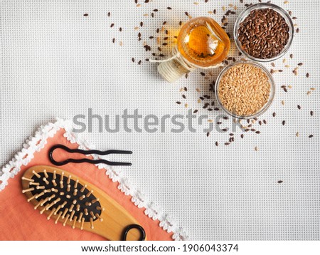 Flaxseed oil and seeds are on a white surface, a comb and hairpins lie next to an orange napkin. Illustration for the use of flax products for beauty and restoration of damaged hair. View from above  Royalty-Free Stock Photo #1906043374