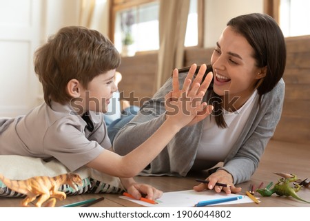 Overjoyed young Caucasian mother and small son give high five celebrate good result have fun drawing together. Smiling mom or nanny painting at home make deal with little boy child. Hobby concept. Royalty-Free Stock Photo #1906044802