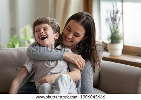 Overjoyed young Caucasian mom and small 7s son have fun play together on weekend in living room. Happy mother feel playful engaged in funny game tickle little boy child. Family entertainment concept. Royalty-Free Stock Photo #1906045666