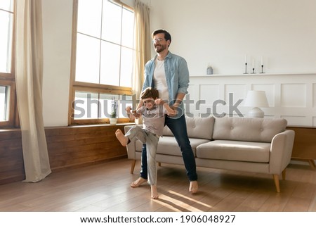 Overjoyed young Caucasian father have fun dance with excited little 7s son in cozy living room. Happy dad engaged in funny game or activity with small boy child, enjoy feel playful on weekend at home.