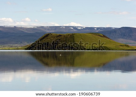Crater reflecting in clear still water of Myvatn lake on a sunny summer day, Iceland