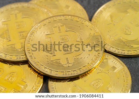 Golden bitcoins placed on top of a pile of coins and facing the camera.
